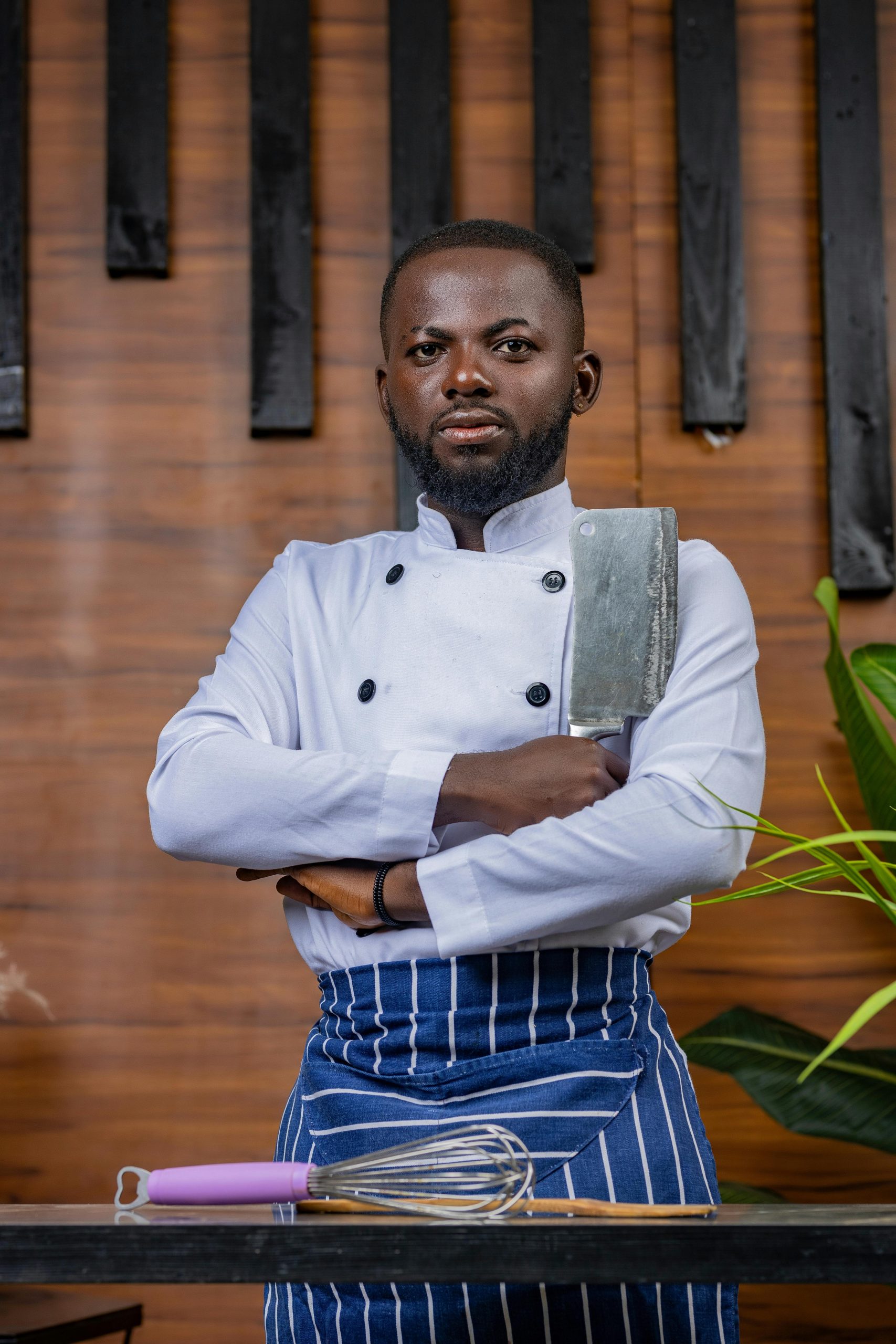 Portrait of a confident chef posing with a cleaver in a stylish kitchen environment.